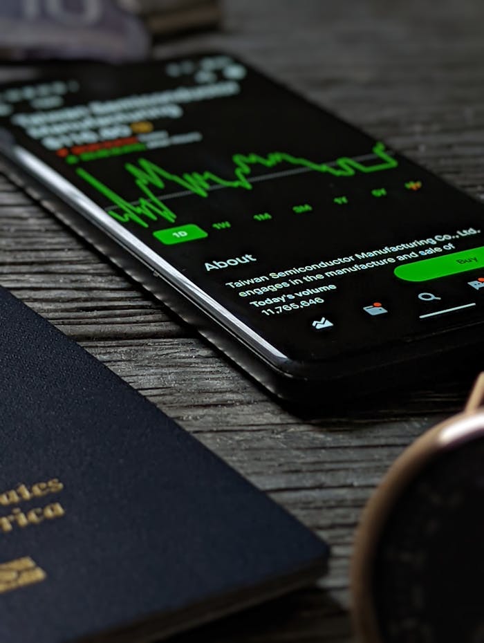 Close-up of a smartphone on a wooden surface displaying a stock market graph next to documents and a watch.